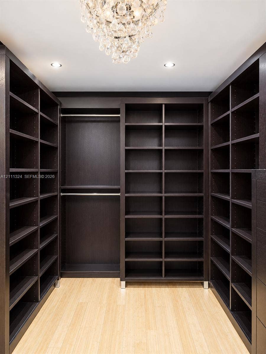 Custom dark-finish built-in shelving, wood-finish flooring, integrated metal hanging rods, and a tiered crystal chandelier