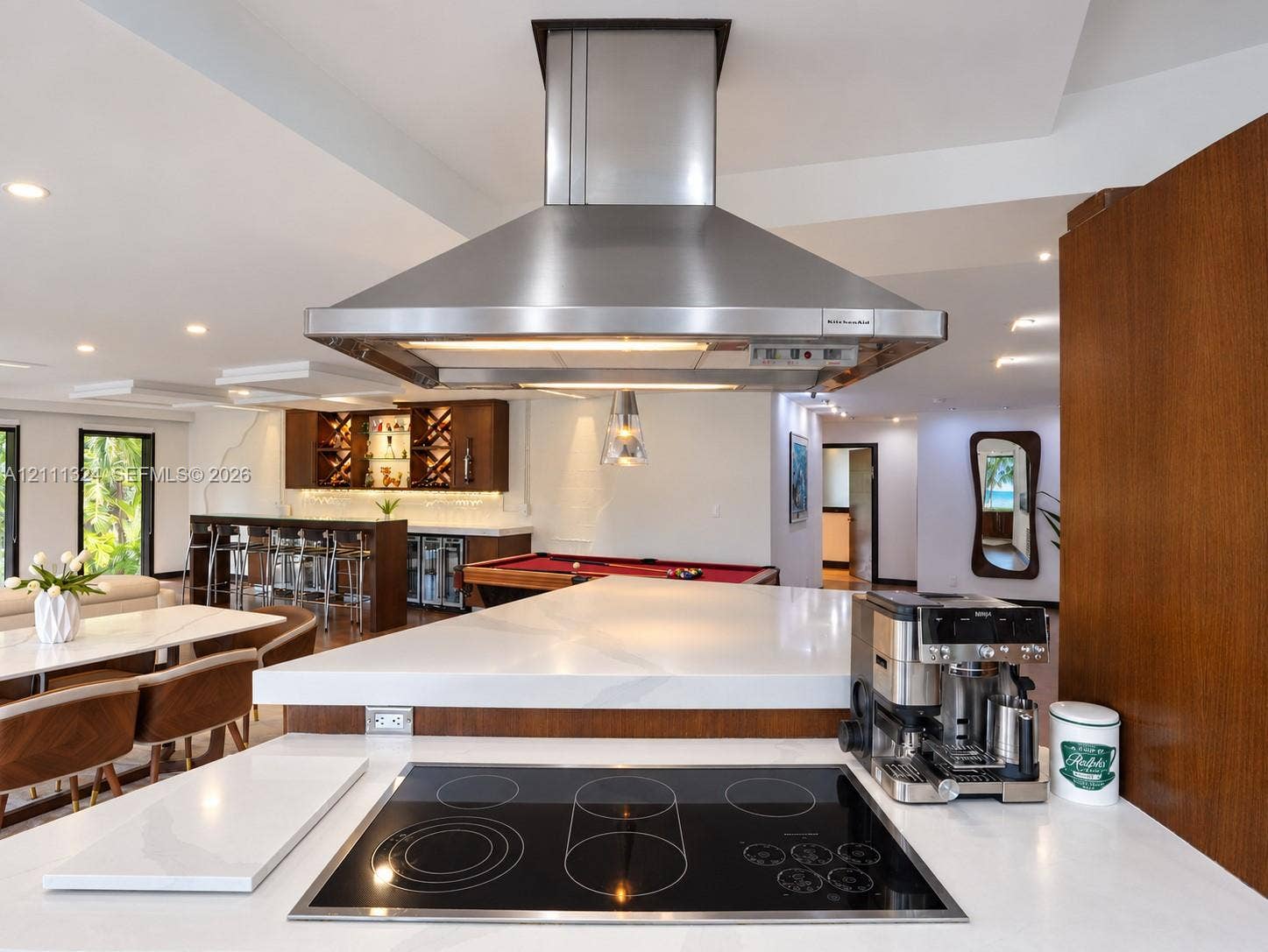 Kitchen featuring a white solid-surface countertop with an integrated electric cooktop, a stainless steel chimney-style range hood, and wood-finish cabinetry
