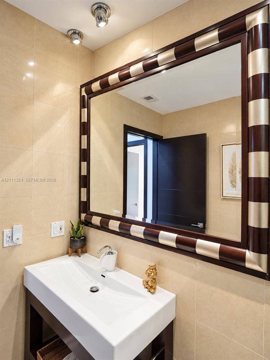 Rectangular white vessel sink atop a dark wood-finish vanity, large wall mirror with a decorative two-tone wood and metal frame, and full-height stone wall tile