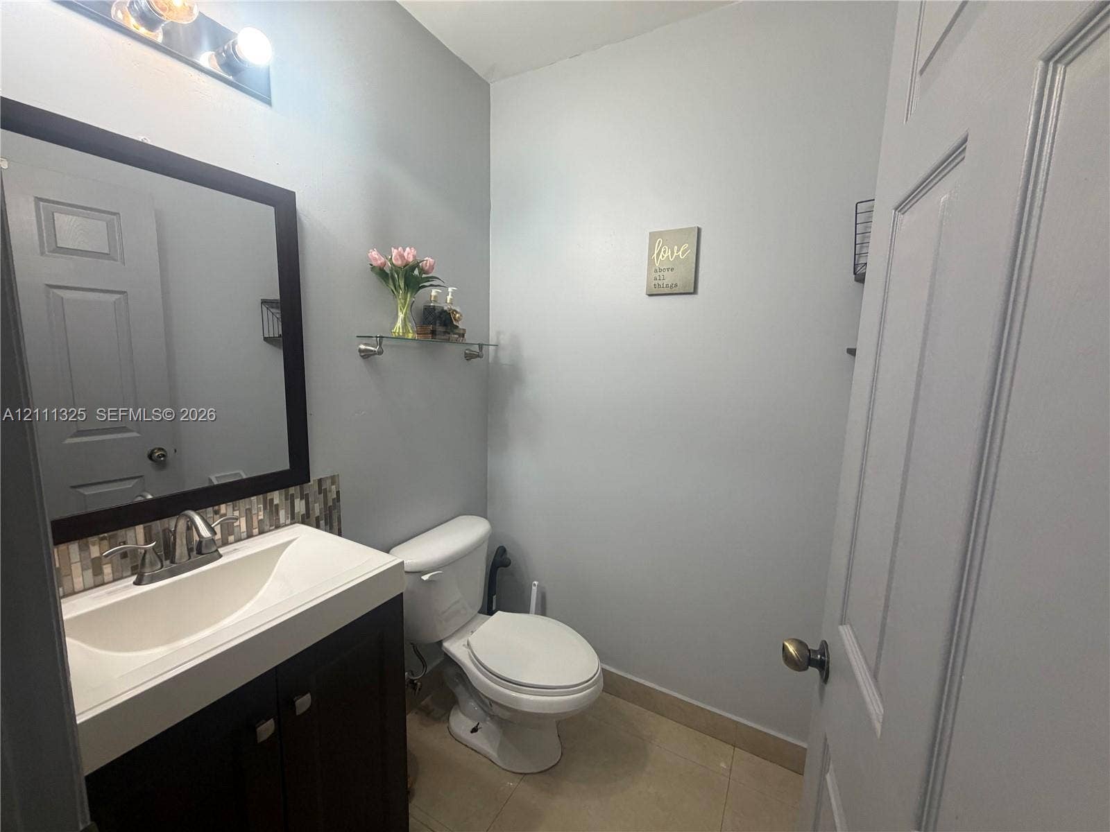 18172 SW 108th Path, Miami, Miami, FL 33157 Dark wood-finish vanity with an integrated basin, glass-tile backsplash, three-light vanity fixture, and neutral tile flooring