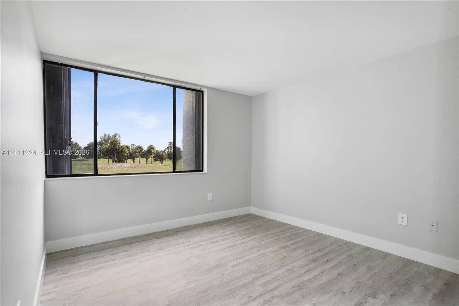 4801 Esedra Court, #207, Lake Worth, FL 33467 Primary bedroom featuring neutral-toned walls, laminate wood-look flooring, and a large horizontal window with a landscape backdrop.