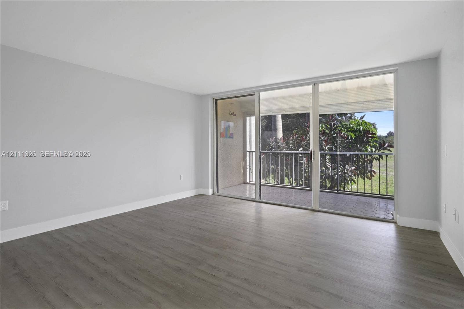 4801 Esedra Court, #207, Lake Worth, FL 33467 Living area featuring wood-look laminate flooring, crisp white walls, and expansive floor-to-ceiling sliding glass doors opening to a private screened-in balcony.