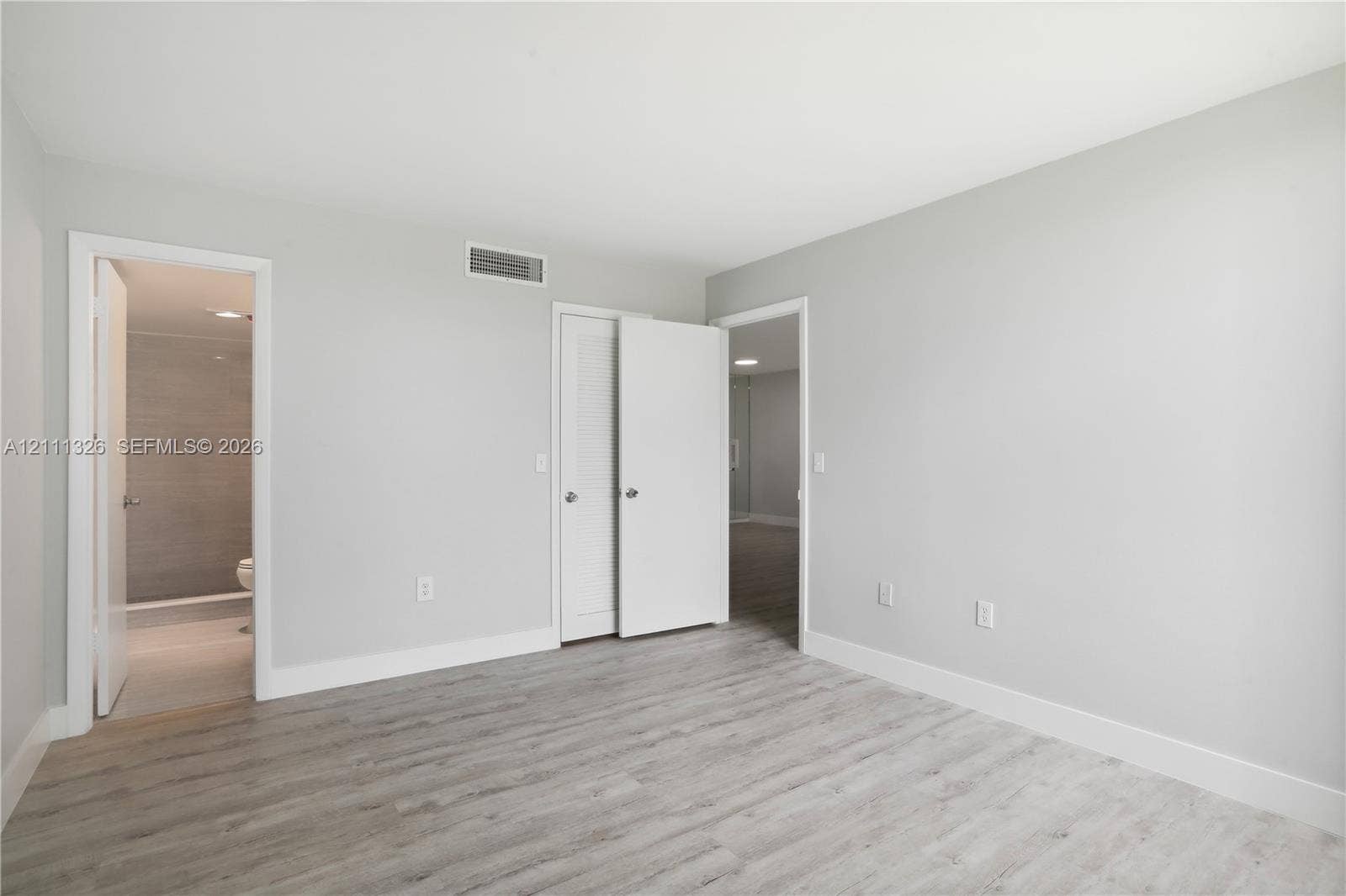 4801 Esedra Court, #207, Lake Worth, FL 33467 Primary bedroom featuring crisp white walls, laminate wood-look flooring, and a walk-in closet and en suite bathroom with a walk-in shower.
