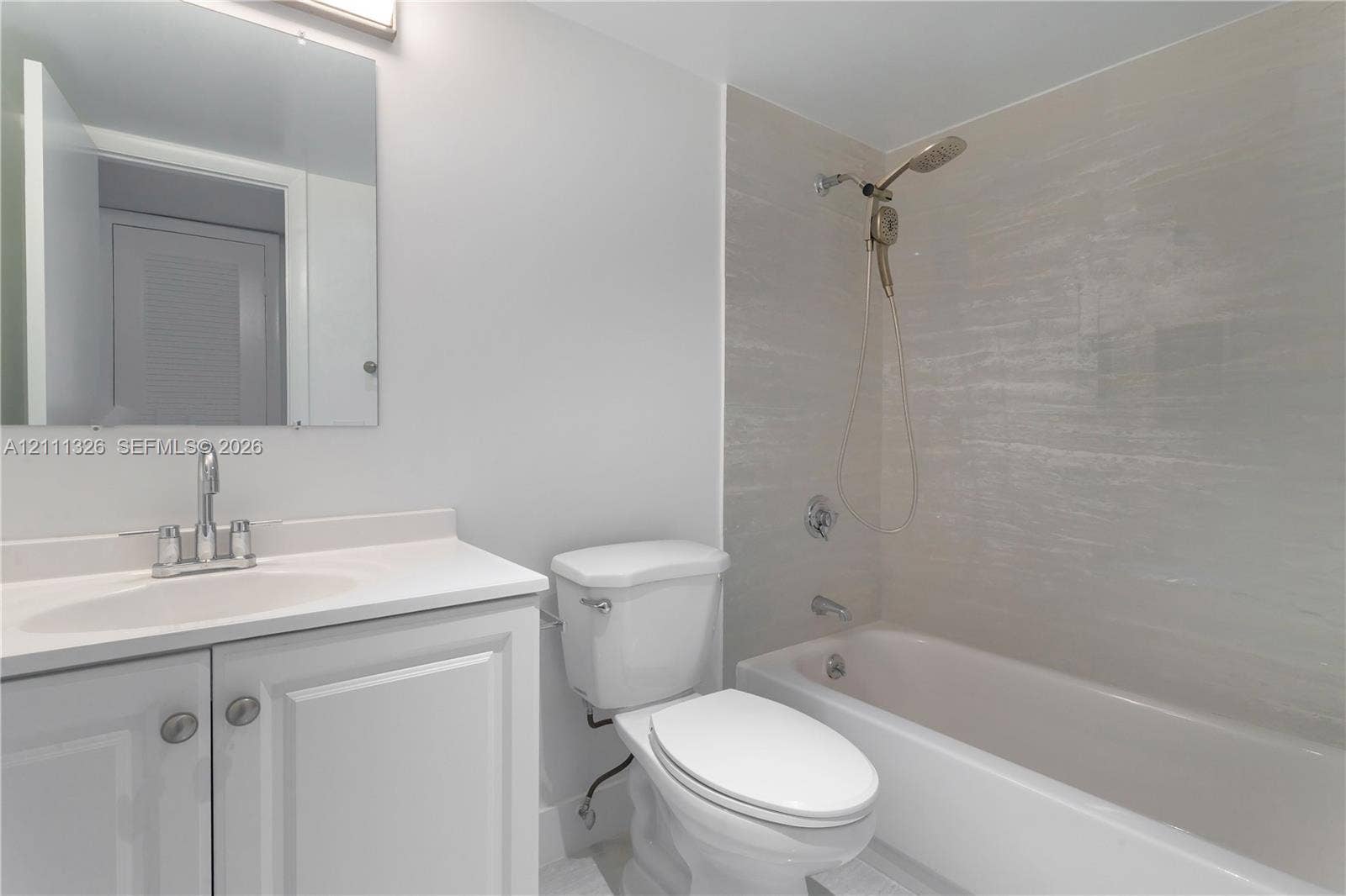 4801 Esedra Court, #207, Lake Worth, FL 33467 Guest bathroom featuring a vanity with an integrated sink, polished chrome faucet, flat-panel cabinetry, a rectangular wall-mounted mirror, and a bathtub with a tiled surround.