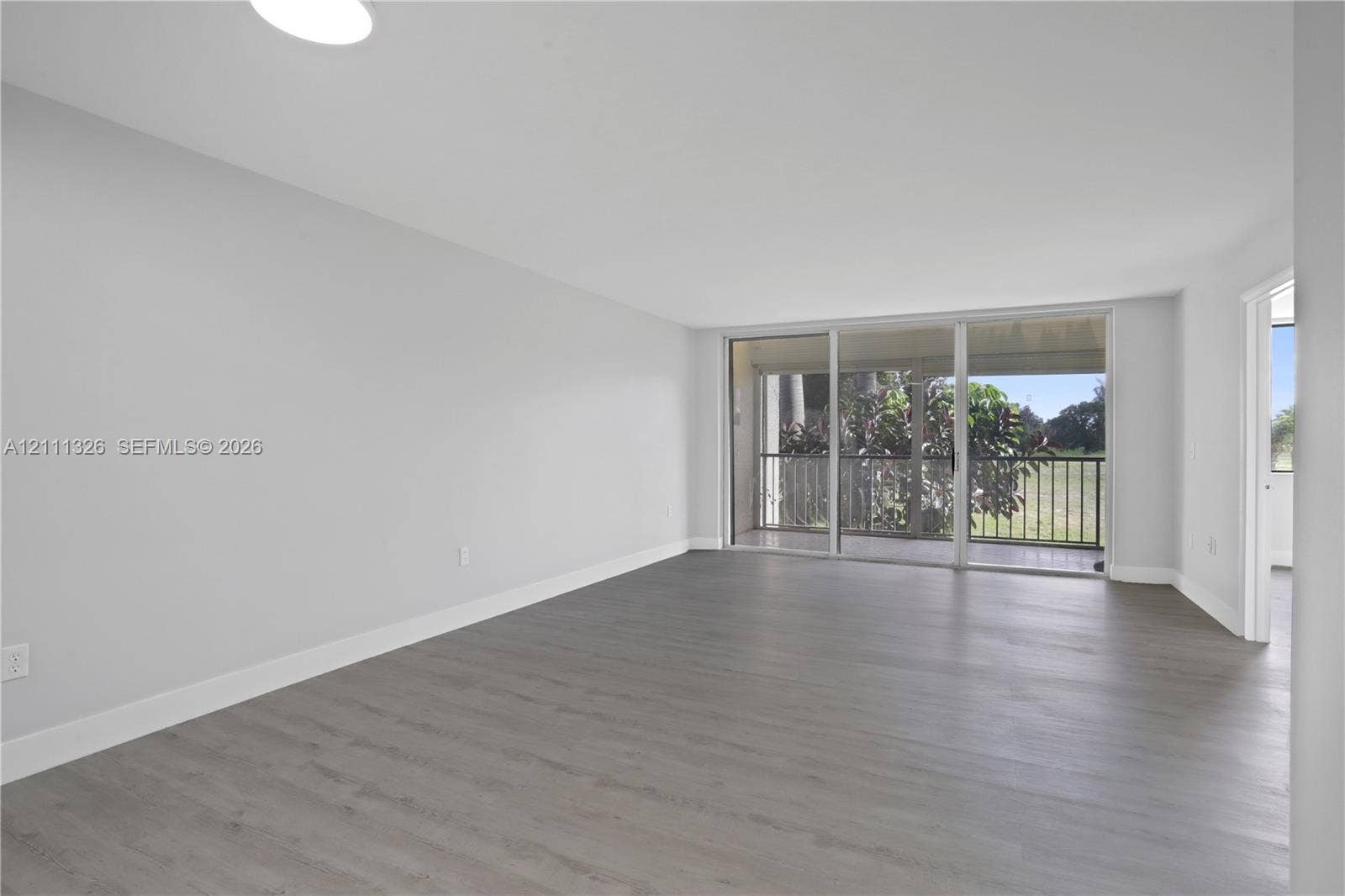 4801 Esedra Court, #207, Lake Worth, FL 33467 Open-concept interior featuring neutral walls, wood-finish flooring, and sliding glass doors leading to a covered screened-in balcony.