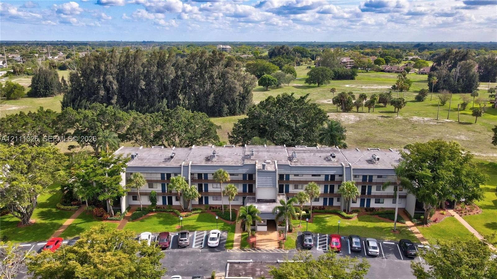 4801 Esedra Court, #207, Lake Worth, FL 33467 Multi-story residential building featuring a concrete facade, integrated parking area, and surrounding green space with mature trees.