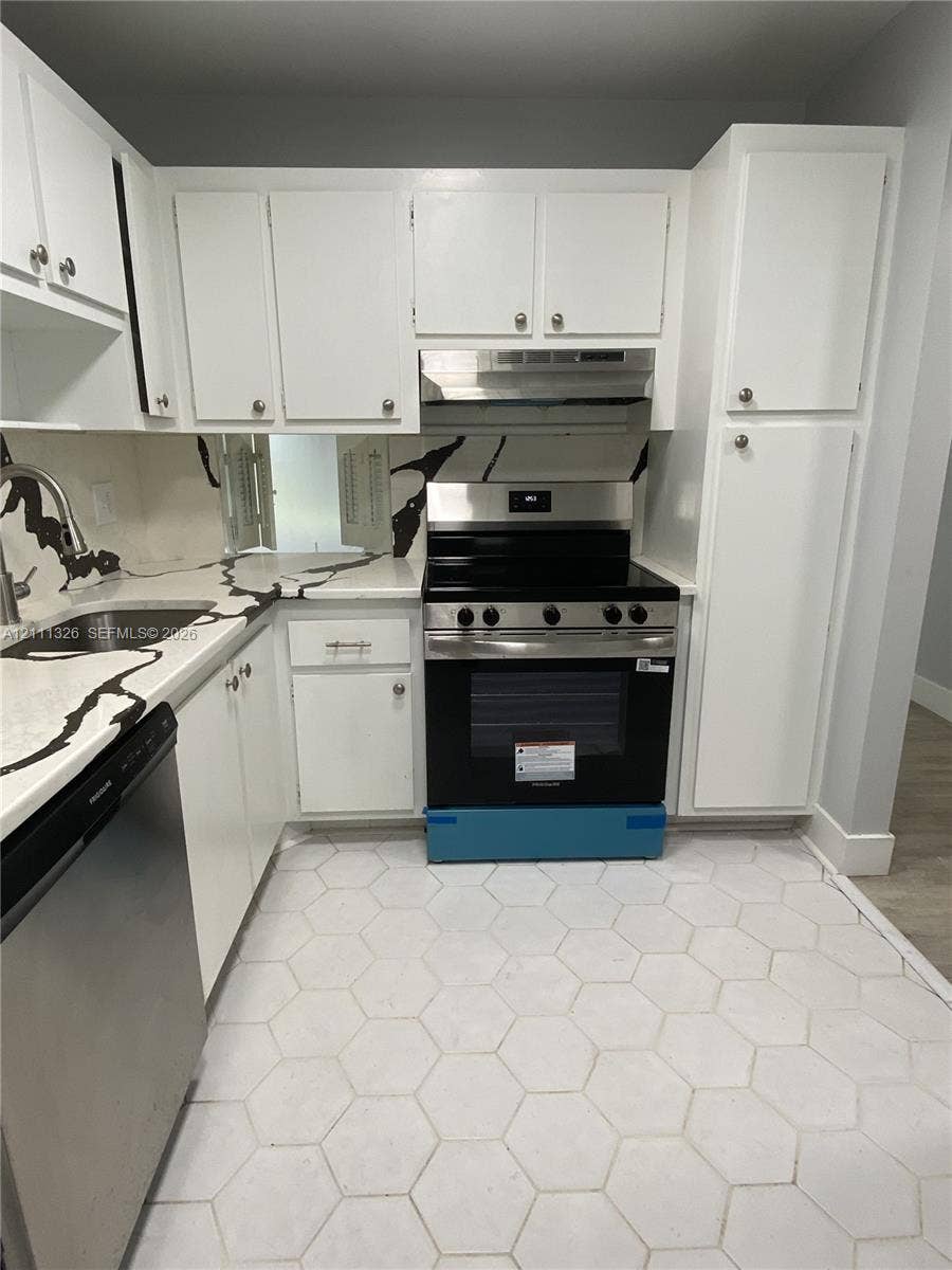 4801 Esedra Court, #207, Lake Worth, FL 33467 Kitchen featuring white shaker-style cabinetry, stainless steel appliances, patterned stone-finish countertops with matching backsplash, hexagonal tile flooring and passthrough to dining area.