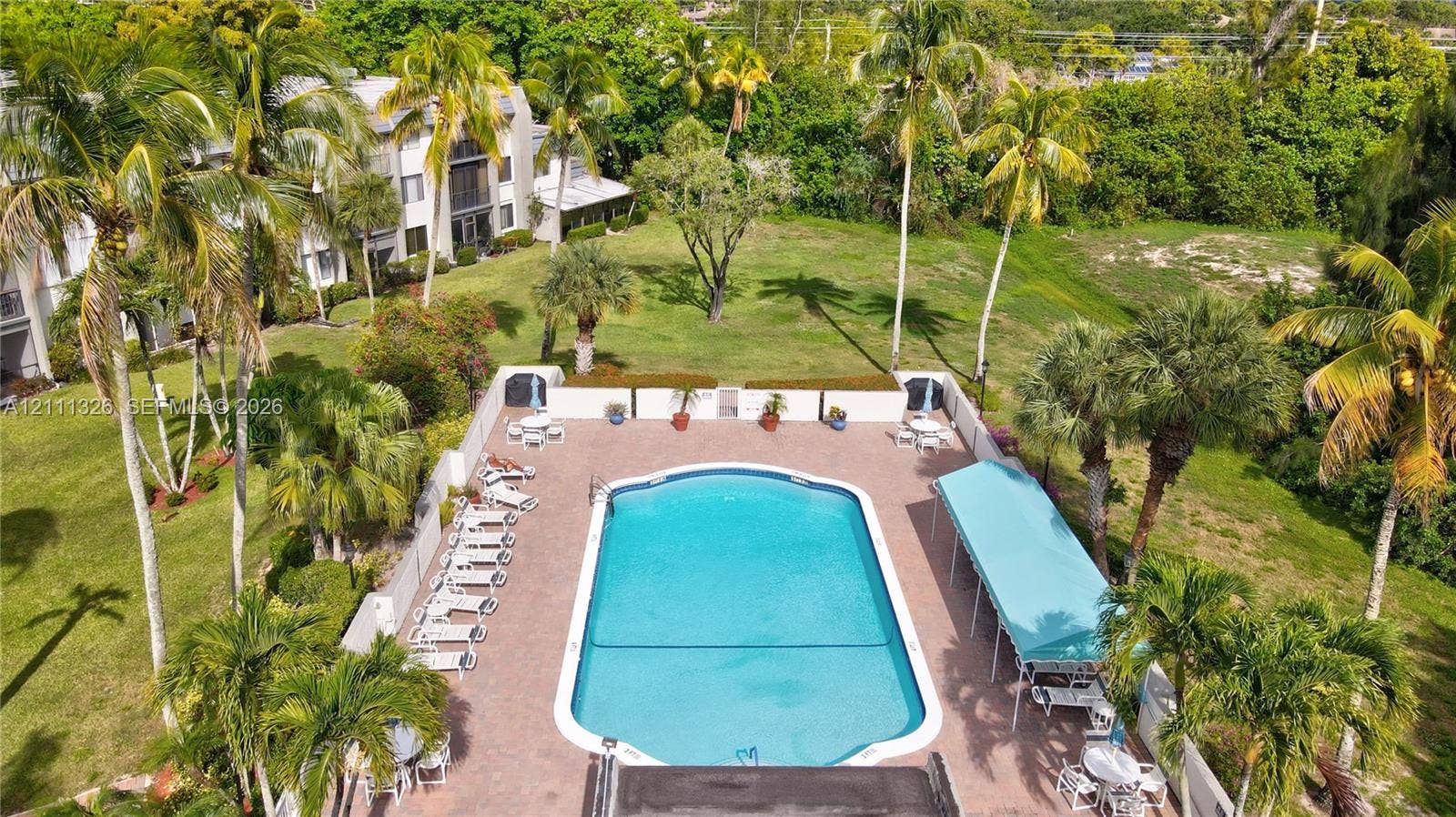 4801 Esedra Court, #207, Lake Worth, FL 33467 Outdoor community swimming pool featuring a paver deck, perimeter fencing, and a covered patio area set within a landscaped property with mature trees.