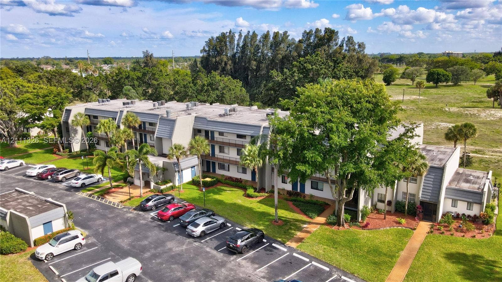 4801 Esedra Court, #207, Lake Worth, FL 33467 Multi-story exterior featuring paved surface parking and manicured landscaping with mature trees.