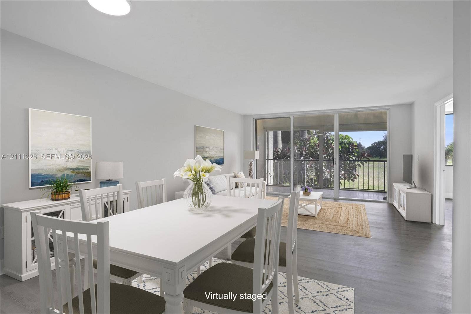 4801 Esedra Court, #207, Lake Worth, FL 33467 Open-concept interior featuring neutral walls, wood-finish flooring, and sliding glass doors leading to a covered screened-in balcony. This photo has been virtually staged.