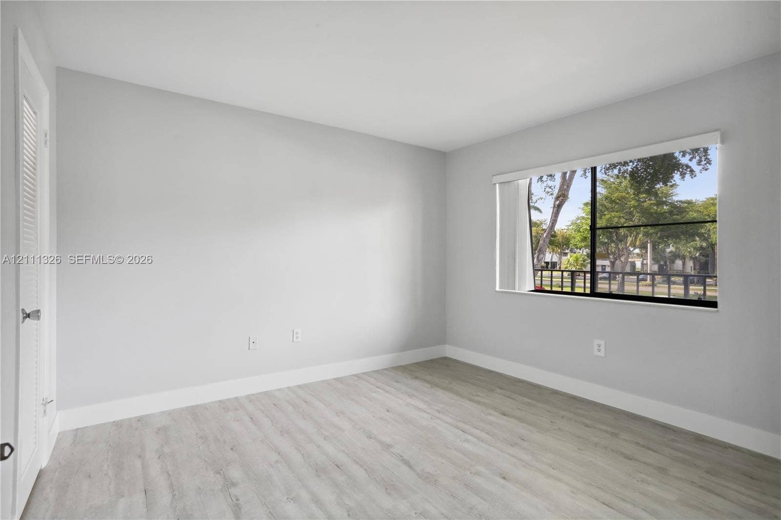 4801 Esedra Court, #207, Lake Worth, FL 33467 Second bedroom with neutral-toned interior featuring wood-look laminate flooring, a large window with black frames, and a walk-in closet.