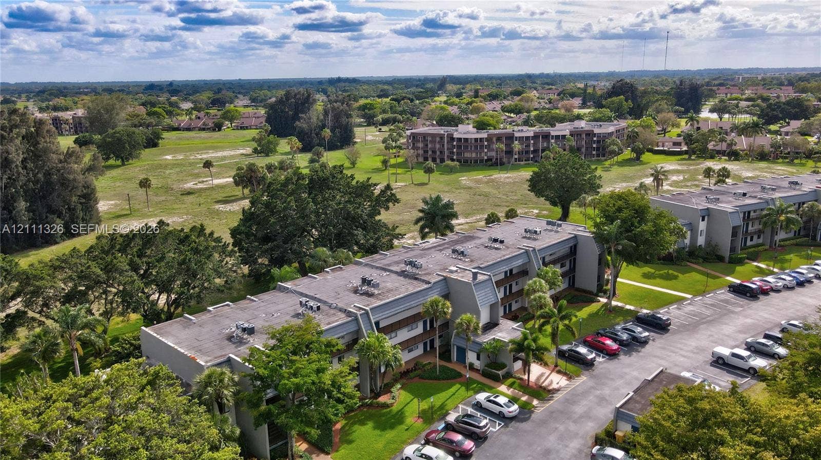 4801 Esedra Court, #207, Lake Worth, FL 33467 Aerial perspective featuring multi-story residential buildings, paved surface parking, manicured landscaping, and mature trees.