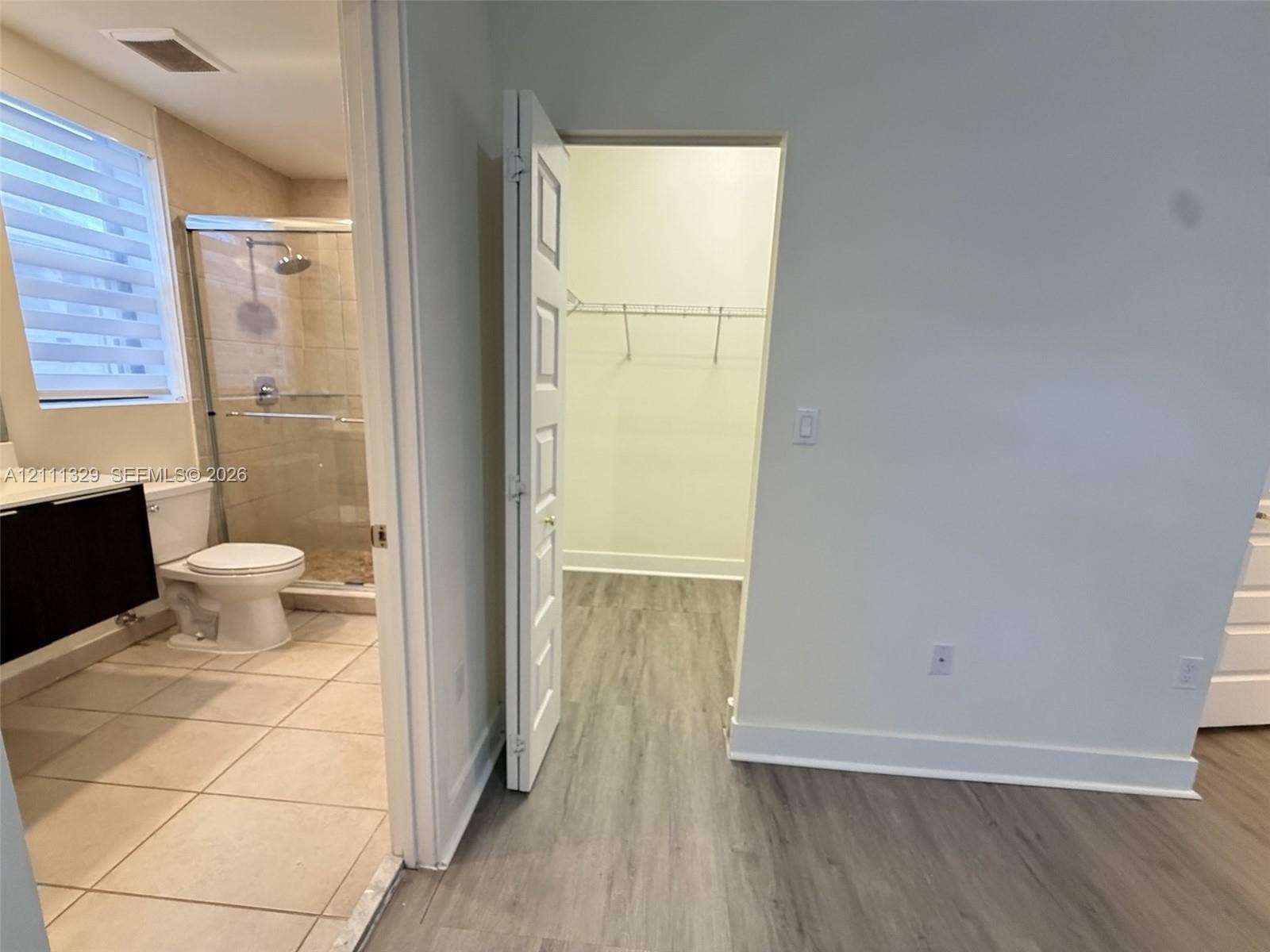 10443 NW 82nd Street, #6, Doral, Doral, FL 33178 Bathroom featuring a shower with a glass enclosure, wood-finish cabinetry, and tiled flooring, accompanied by a walk-in closet with built-in wire shelving