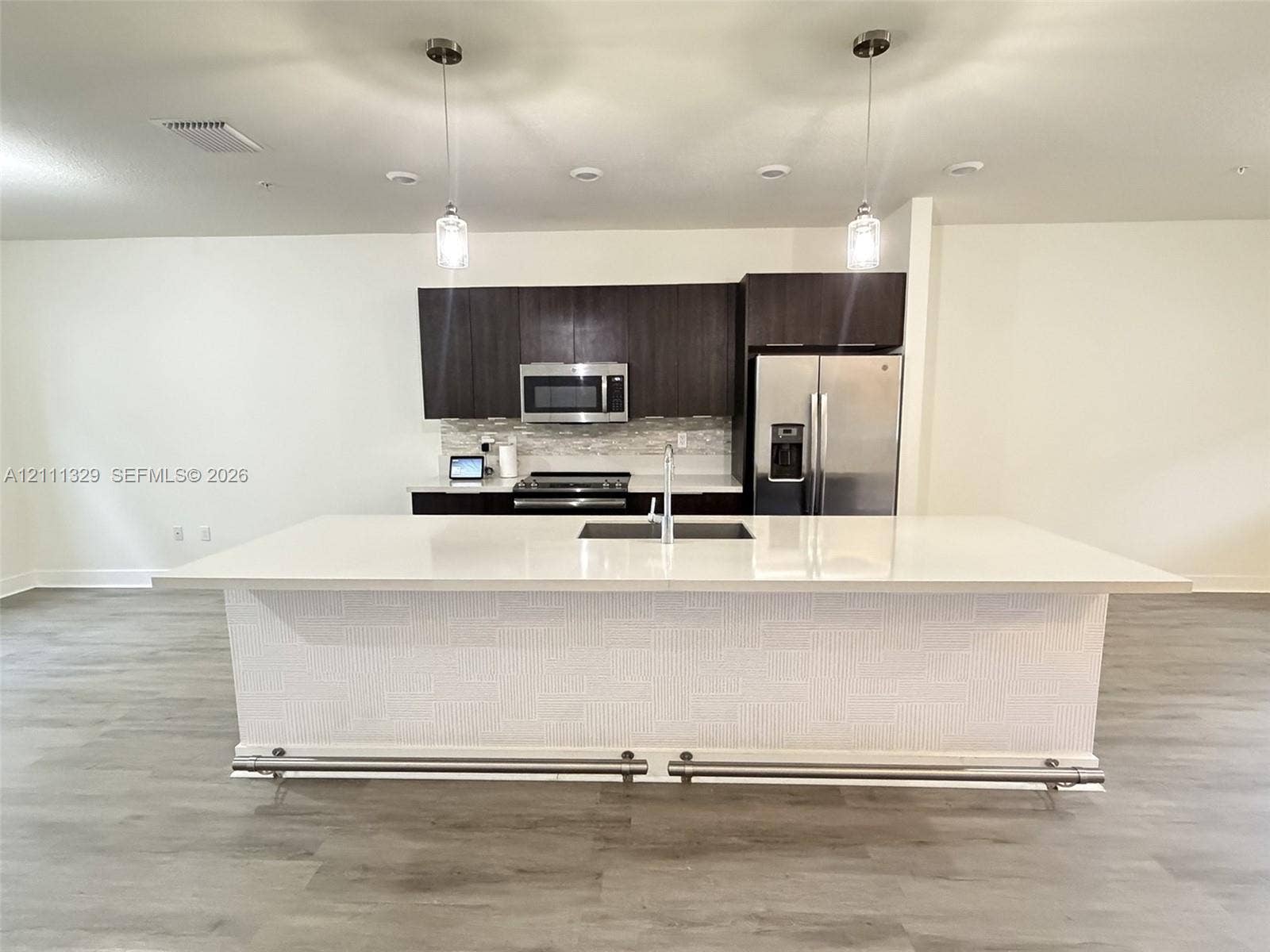 10443 NW 82nd Street, #6, Doral, Doral, FL 33178 Kitchen featuring an expansive island with a solid-surface countertop, dark cabinetry, stainless steel appliances, textured island base finish, and pendant lighting