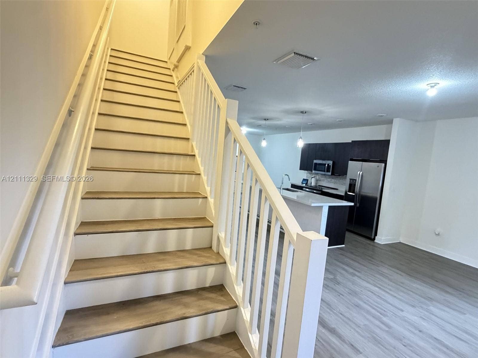 10443 NW 82nd Street, #6, Doral, Doral, FL 33178 Staircase with wood-finish treads and white balusters, leading to an open-concept kitchen featuring dark cabinetry, an island with a light-toned countertop, and stainless steel appliances