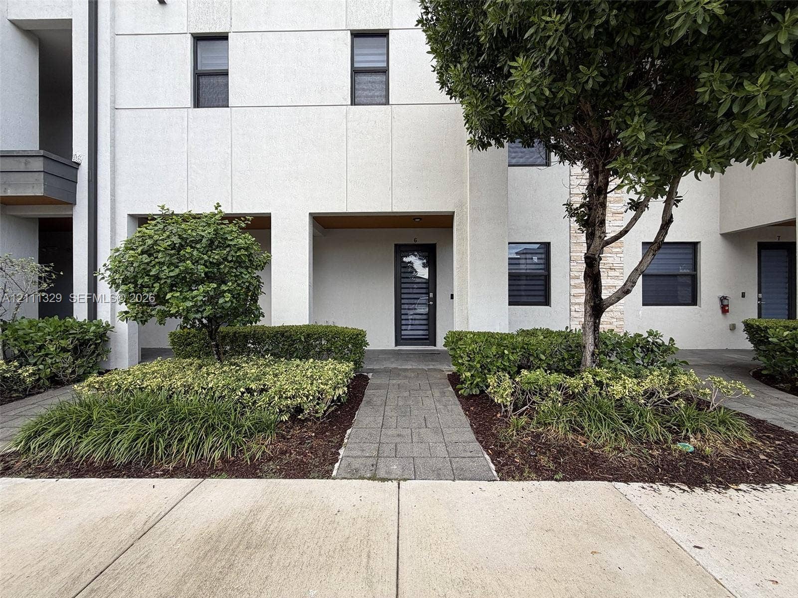 10443 NW 82nd Street, #6, Doral, Doral, FL 33178 Modern facade with panelized exterior, multi-pane entry door, stone-clad accent wall, stone paver walkway, and manicured shrubbery