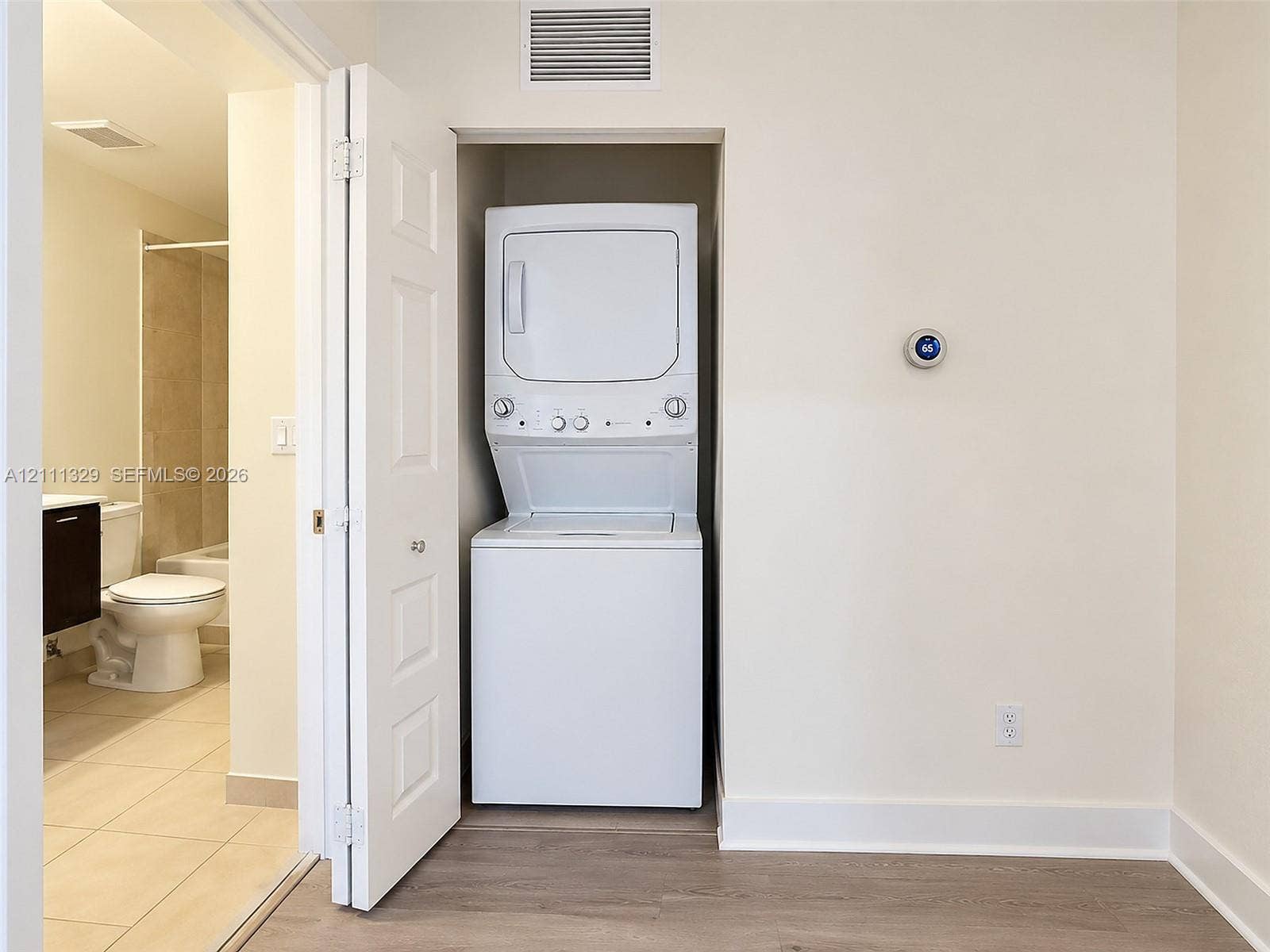 10443 NW 82nd Street, #6, Doral, Doral, FL 33178 Laundry closet featuring a stackable washer and dryer unit, white six-panel bifold door, digital thermostat, and wood-finish flooring