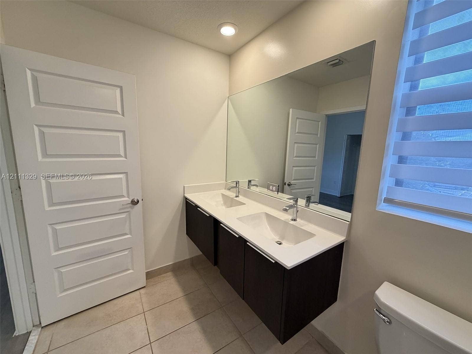 10443 NW 82nd Street, #6, Doral, Doral, FL 33178 Floating dual-sink vanity with dark cabinetry, white solid-surface countertop, chrome fixtures, and a wall-to-wall mirror