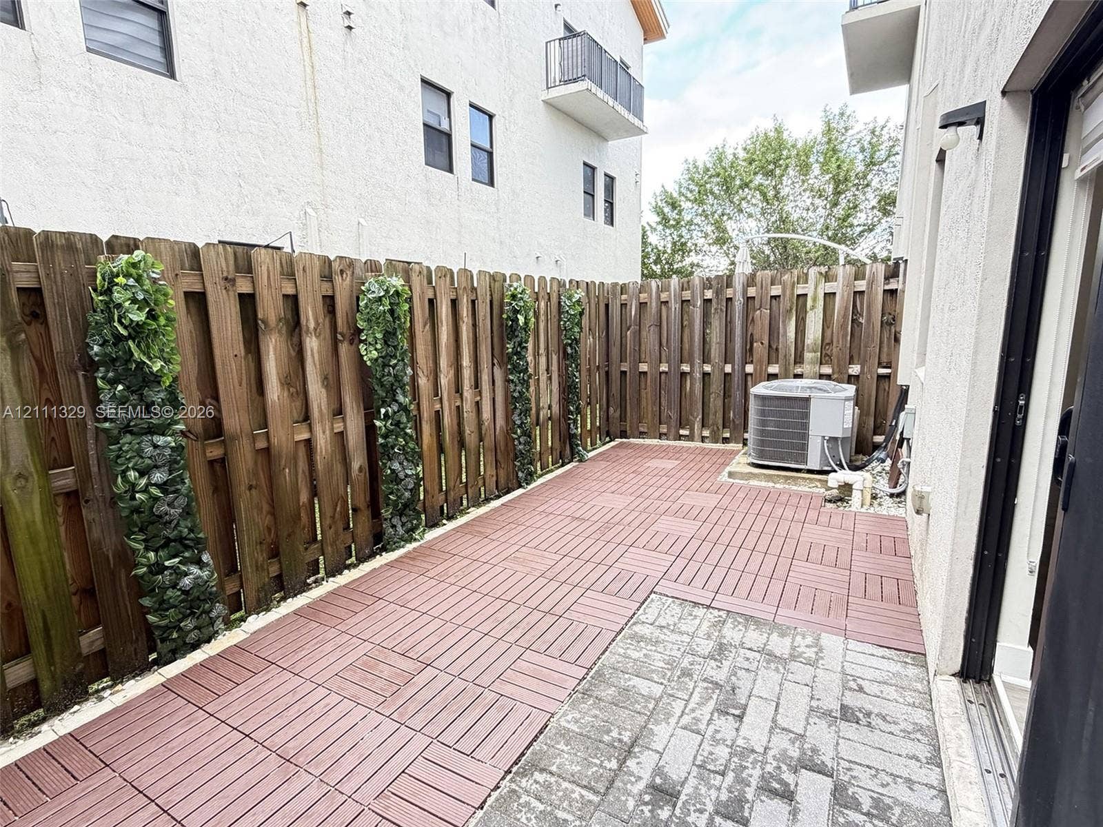 10443 NW 82nd Street, #6, Doral, Doral, FL 33178 Private patio area featuring modular composite decking, gray stone paver accents, and a full-perimeter wood privacy fence