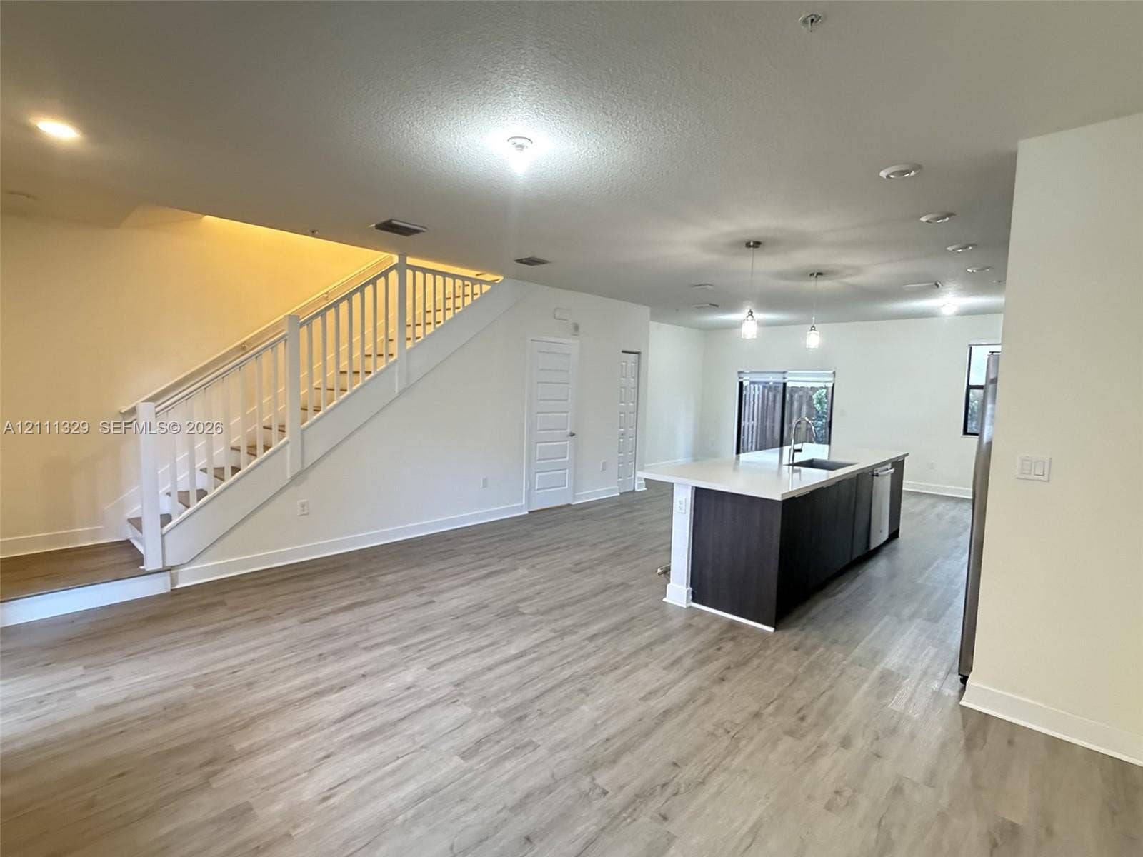 10443 NW 82nd Street, #6, Doral, Doral, FL 33178 Open-concept interior featuring wood-finish flooring, a kitchen island with quartz countertops, custom cabinetry, pendant lighting, and a staircase with white balusters