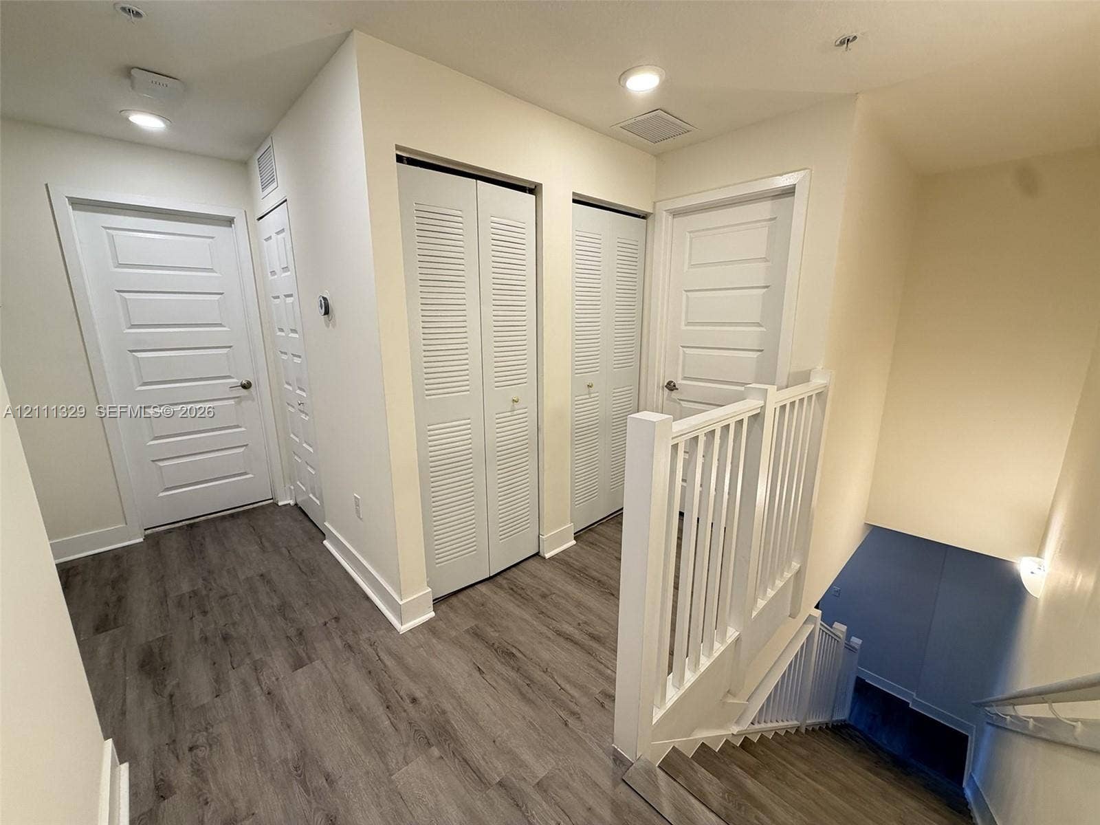 10443 NW 82nd Street, #6, Doral, Doral, FL 33178 Hallway featuring wood-finish flooring, two sets of louvered-panel closet doors, recessed lighting, and a white balustrade staircase railing