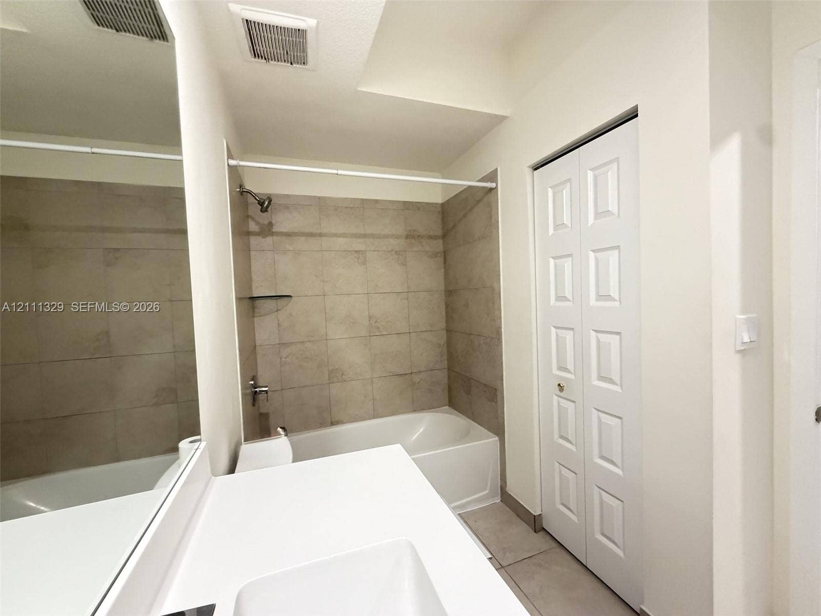 10443 NW 82nd Street, #6, Doral, Doral, FL 33178 Full-width vanity with a rectangular basin, expansive wall-mounted mirror, white six-panel bifold closet door, and bathtub featuring neutral-toned wall tile