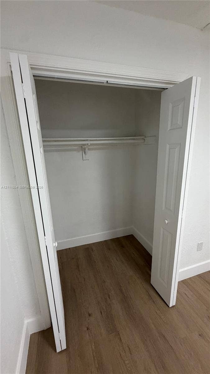 3314 NW 8th, #1, Miami, Miami, FL 33131 Closet featuring white bi-fold doors and integrated shelf with hanging rod, complemented by wood-finish flooring
