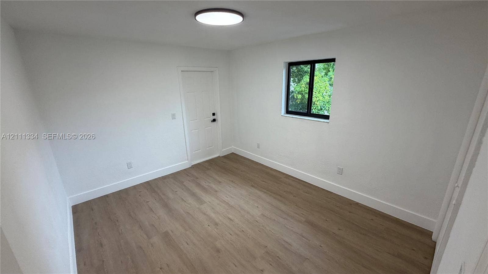 3314 NW 8th, #1, Miami, Miami, FL 33131 Interior space featuring wood-finish flooring, a flush-mount ceiling light fixture, a single-panel door, and a black-framed window