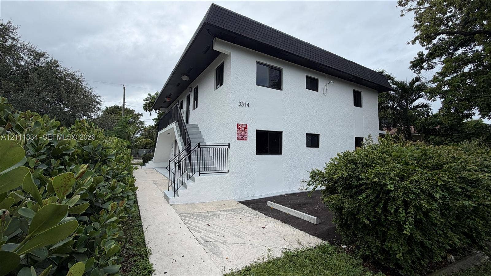 3314 NW 8th, #1, Miami, Miami, FL 33131 Two-story exterior featuring white stucco siding, a flat roofline, black metal handrails, and surface-level parking