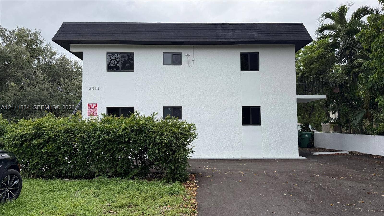 3314 NW 8th, #1, Miami, Miami, FL 33131 Two-story exterior featuring a textured white stucco facade, a dark mansard-style roofline, and asphalt paving