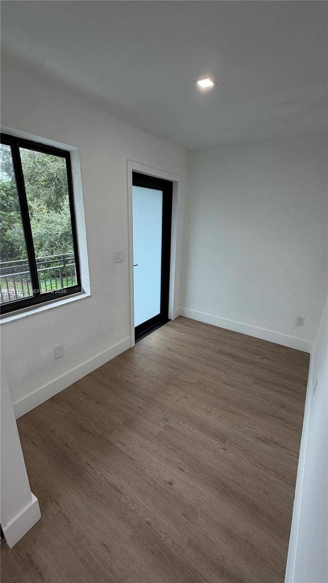3314 NW 8th, #1, Miami, Miami, FL 33131 Neutral-toned wood-finish flooring, single-hung window with black framing, glass-paneled door with black frame, and recessed ceiling lighting