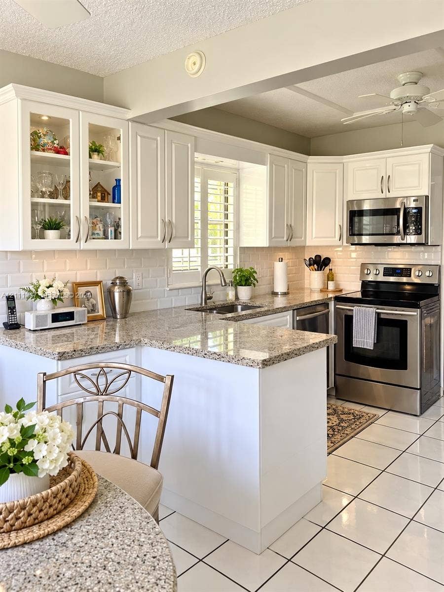 White cabinetry with glass-front uppers, stone-finish countertops, subway tile backsplash, stainless steel appliances, and tiled flooring