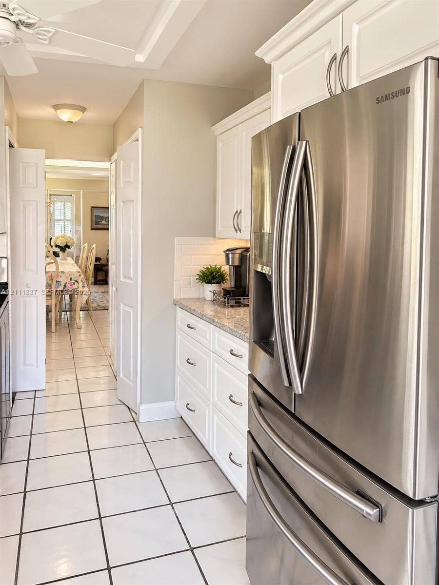 Kitchen featuring white shaker-style cabinetry, stone-finish countertops, subway tile backsplash, stainless steel refrigerator, and tiled flooring