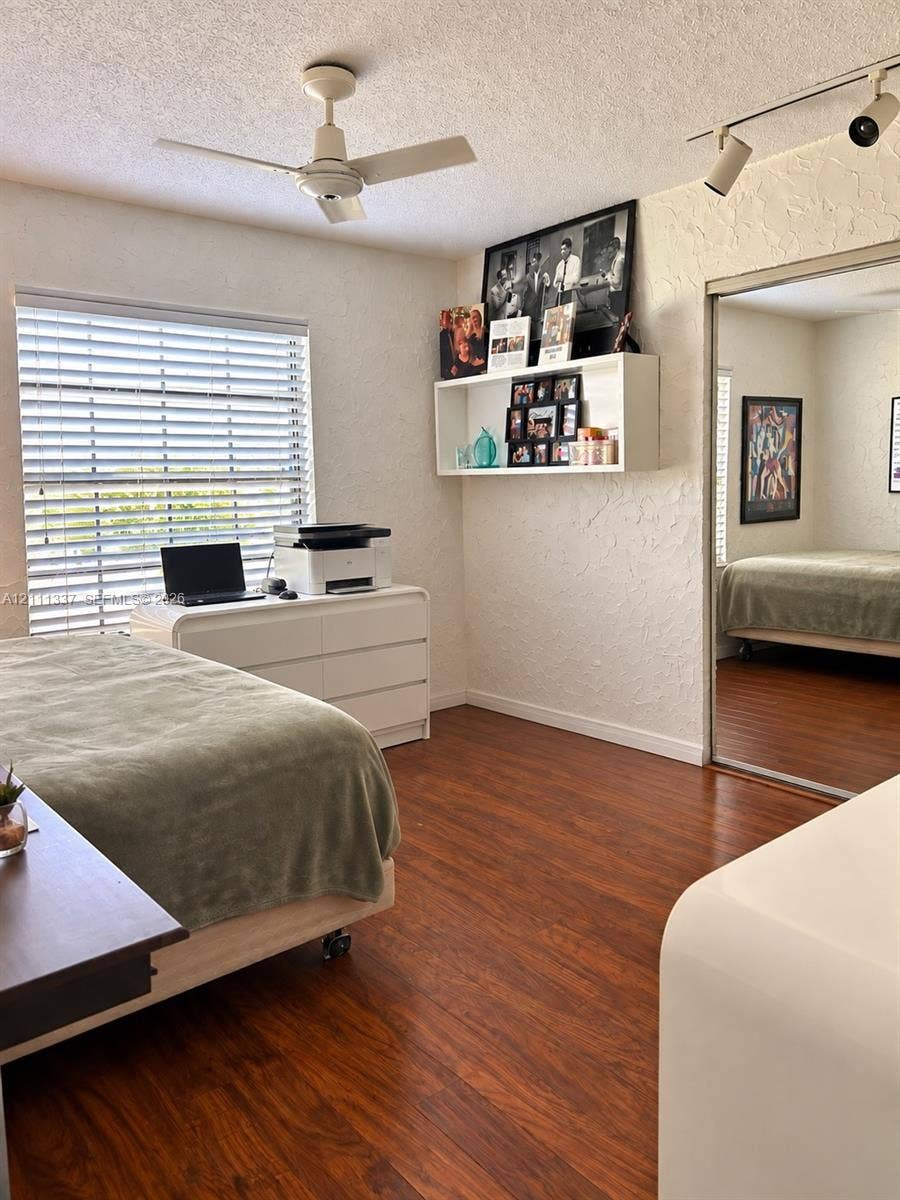 Wood-finish flooring, mirrored closet doors, ceiling fan with integrated lighting, wall-mounted display shelving, and adjustable track lighting