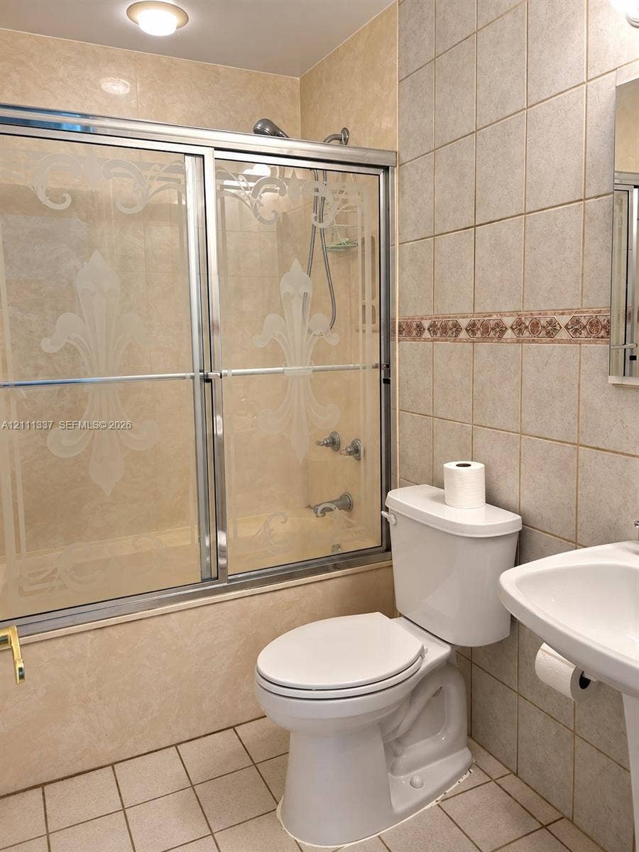 Shower enclosure with decorative etched glass doors, ceramic wall tiling featuring a detailed border accent, and a pedestal sink