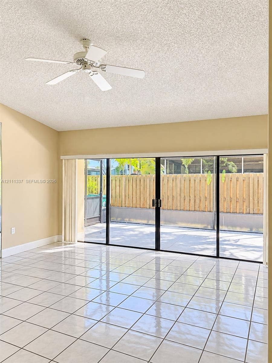 Large-format sliding glass doors, white ceramic tile flooring, and ceiling fan with integrated lighting