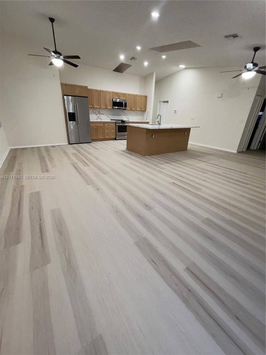 3330 SW 1st Street, Deerfield Beach, Deerfield Beach, FL 33442 Open-concept area featuring light-toned wood-finish flooring, vaulted ceilings with recessed lighting, a central island with a stone-surface countertop, stainless steel appliances, and shaker-style cabinetry