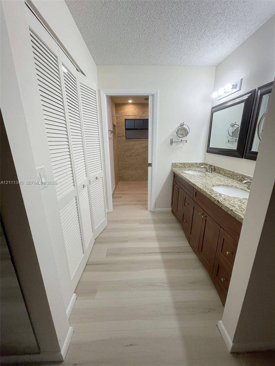 3330 SW 1st Street, Deerfield Beach, Deerfield Beach, FL 33442 Dual-sink vanity with stone-finish countertop, wood-finish cabinetry, louvered-style closet doors, and wood-finish flooring