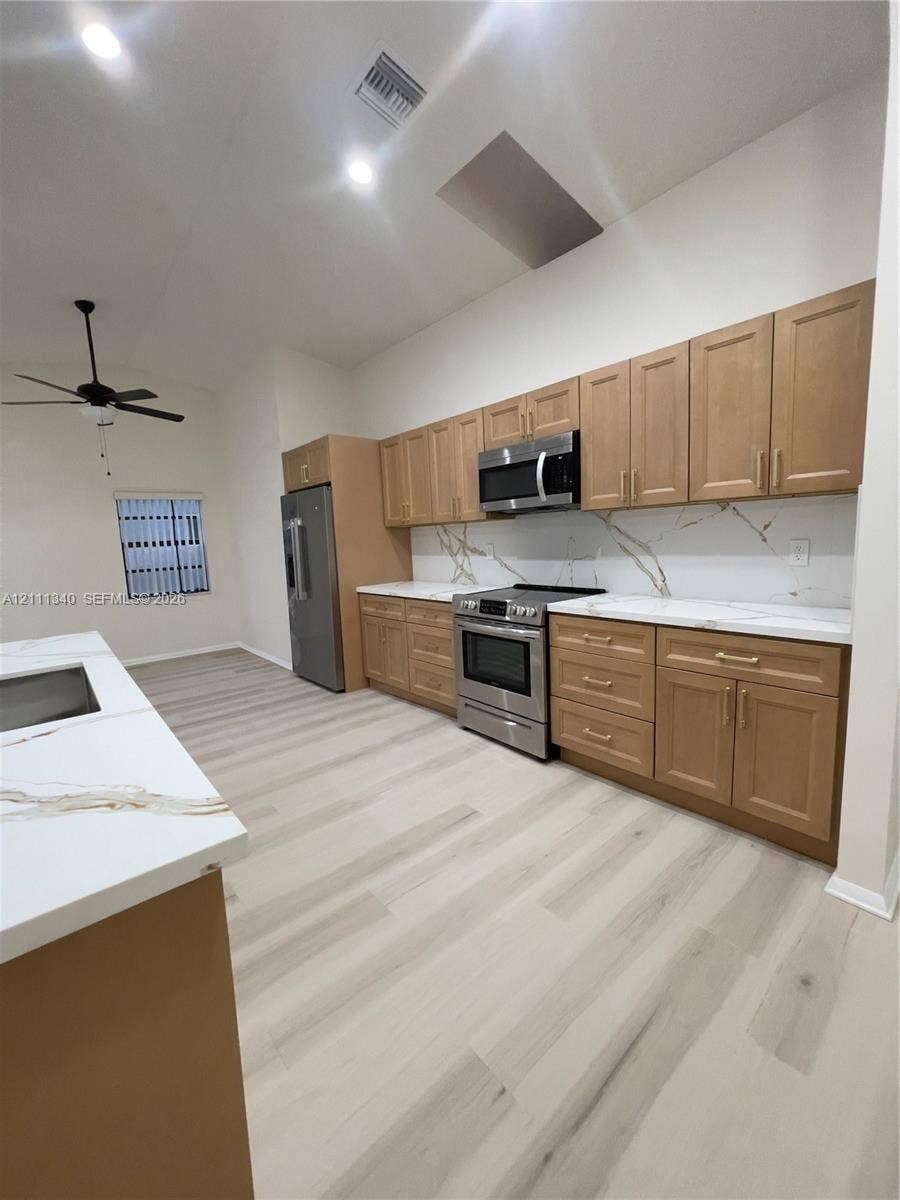 3330 SW 1st Street, Deerfield Beach, Deerfield Beach, FL 33442 Kitchen featuring shaker-style wood cabinetry, stainless steel appliances, stone-finish countertops with waterfall edge detailing, veined stone-style backsplash, and wood-finish flooring