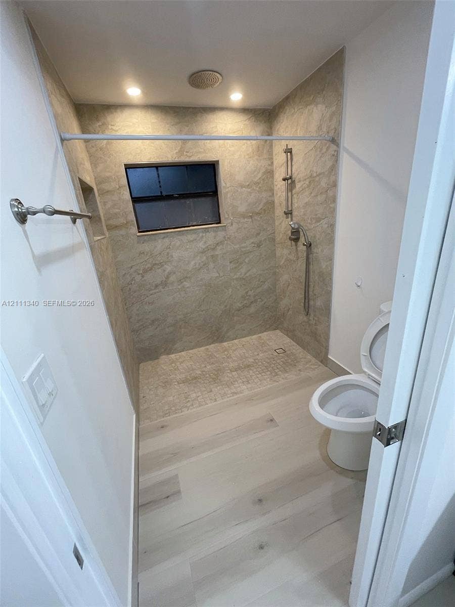 3330 SW 1st Street, Deerfield Beach, Deerfield Beach, FL 33442 Walk-in shower featuring floor-to-ceiling stone-finish tile surround, recessed wall niche, adjustable handheld shower fixture, and light-toned wood-finish flooring