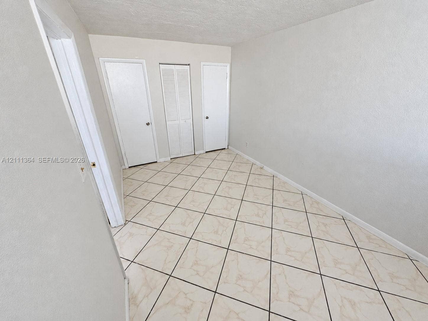 Room featuring diagonal-set tile flooring, neutral wall finishes, and three interior doors including a central louvered-panel closet