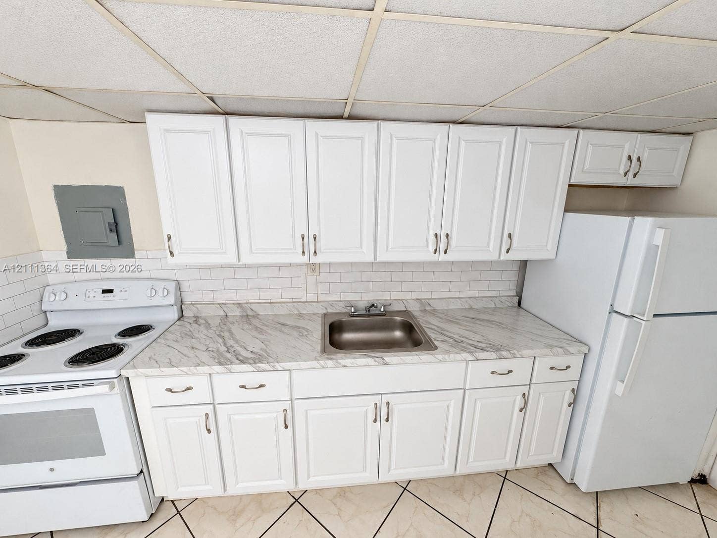 Kitchen featuring white shaker-style cabinetry, stone-patterned laminate countertops, white subway tile backsplash, stainless steel sink, and ceramic tile flooring