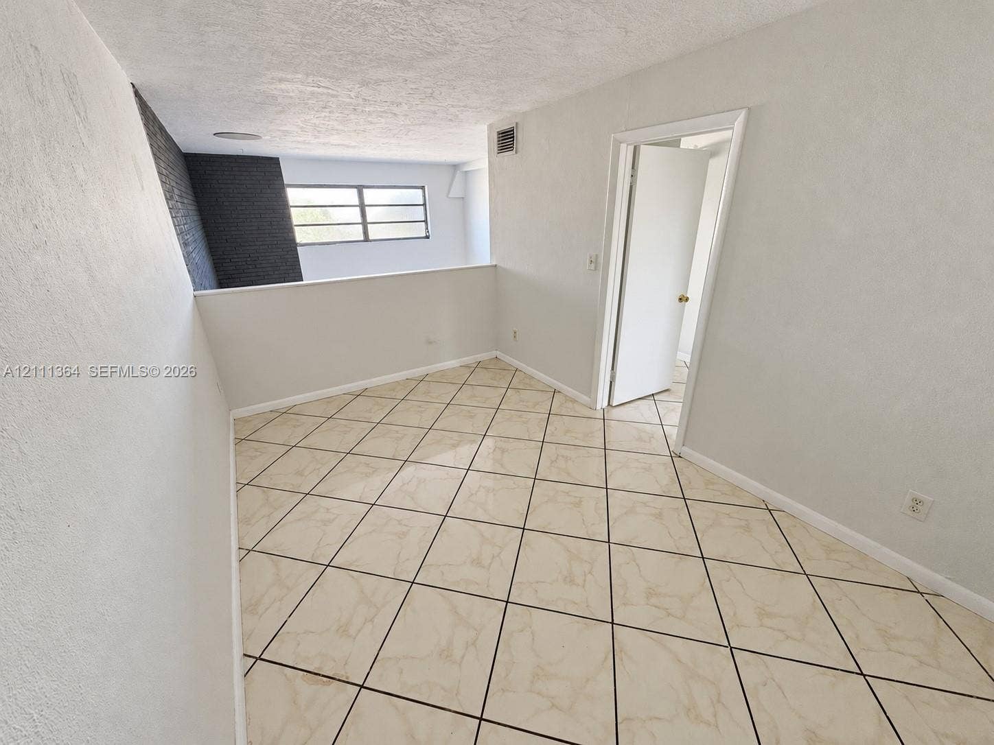 Interior space featuring diagonal tile flooring, a charcoal-toned textured brick accent wall, and a multi-pane window