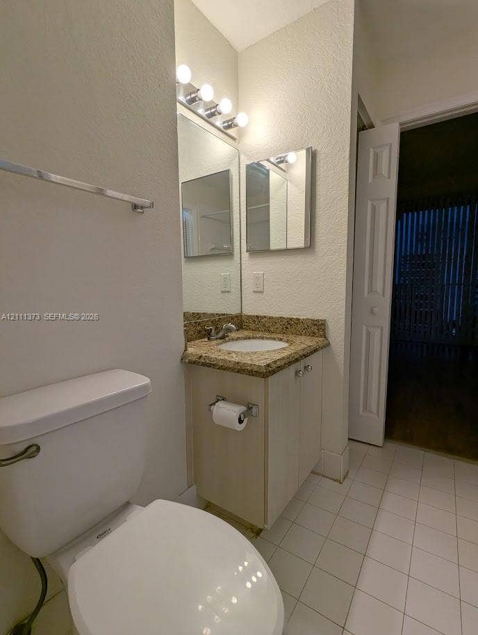 1801 N Flagler Drive, #912, West Palm Beach, West Palm Beach, FL 33401 Single-sink vanity with a stone-finish countertop, white cabinetry, wall-mounted mirror, four-bulb vanity lighting, and white tile flooring