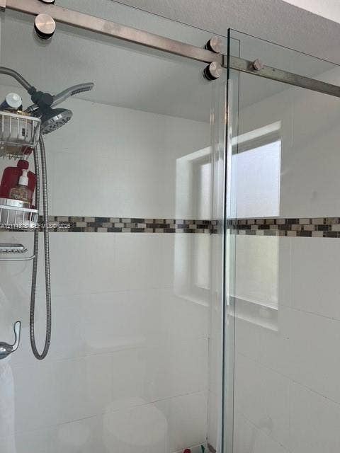 Frameless glass shower enclosure with stainless steel sliding hardware, white wall tile, mosaic tile accent inlay, and adjustable handheld shower head