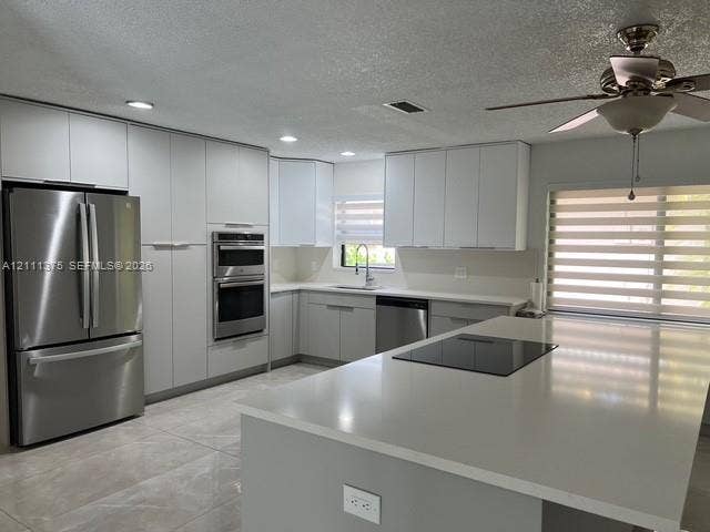 Kitchen featuring white cabinetry, an expansive quartz island with a built-in cooktop, stainless steel appliances including a double wall oven, and large-format tile flooring