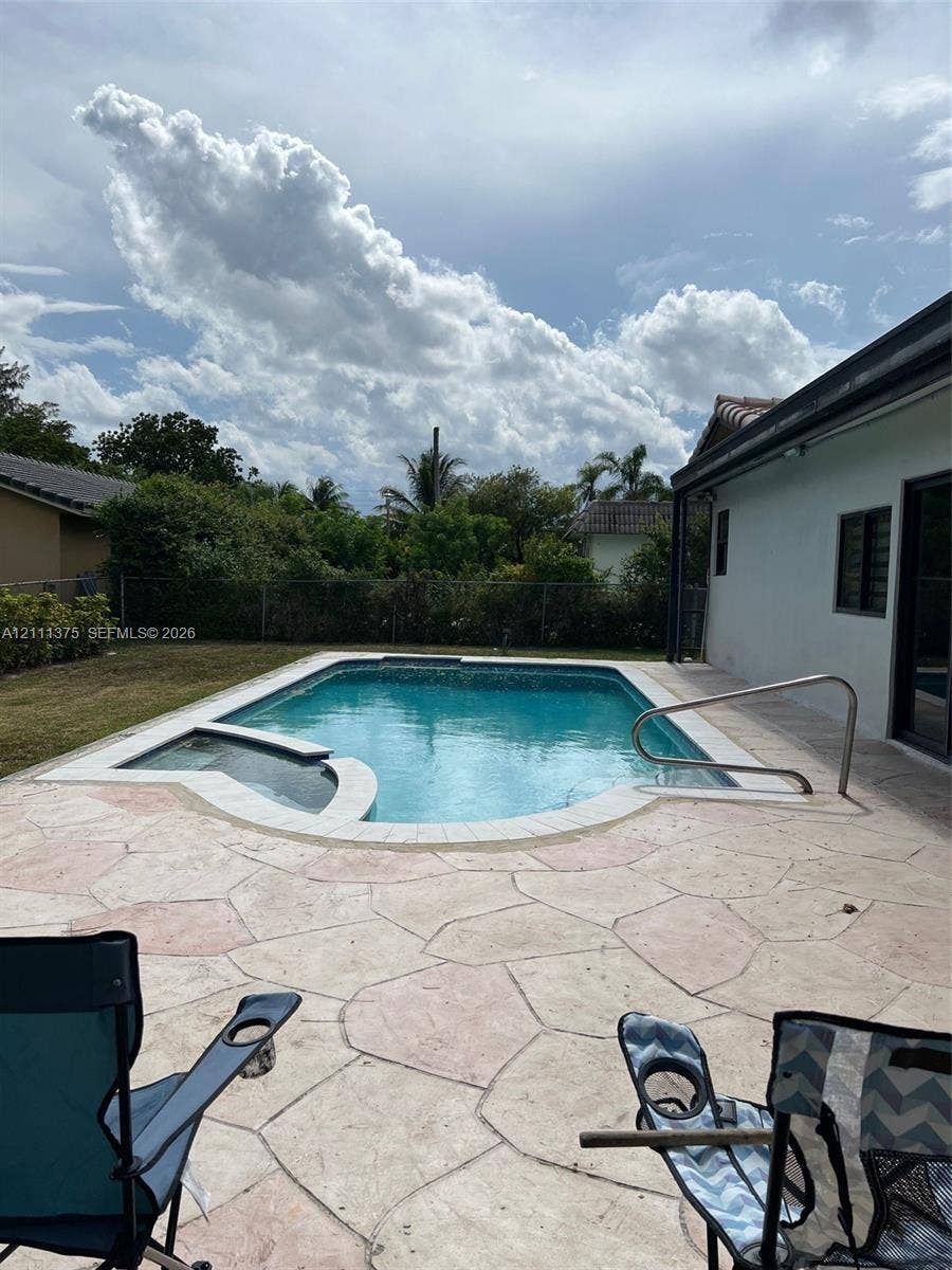 In-ground swimming pool with integrated spa, bordered by an expansive flagstone patio, metal perimeter fencing, and mature landscape