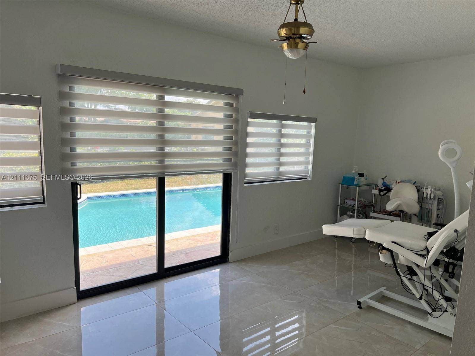 Large format tile flooring, sliding glass door with dual-tone horizontal blinds, and access to an outdoor swimming pool