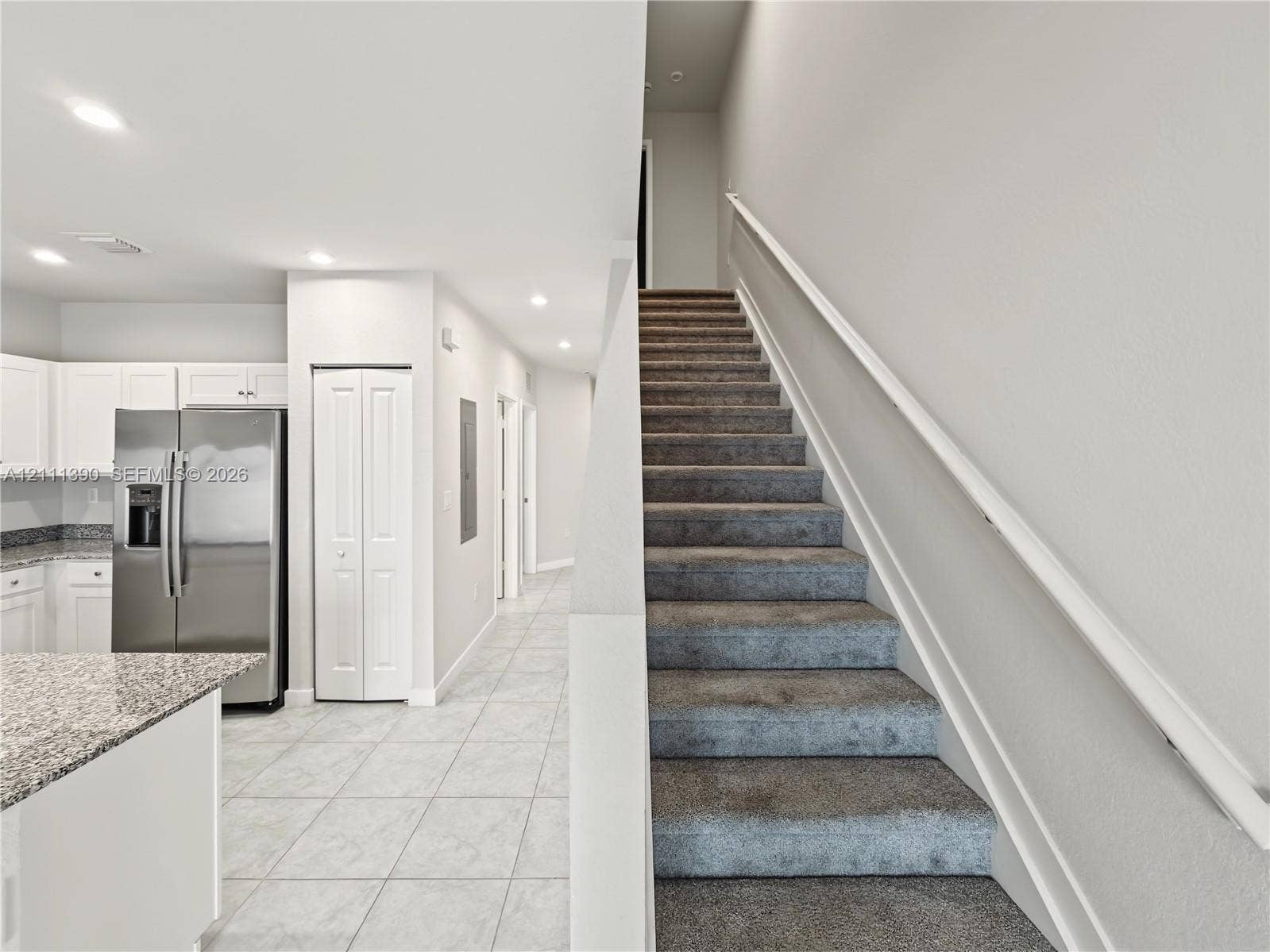 1074 NW 6th Terrace, Florida City, Florida City, FL 33034 Kitchen featuring stainless steel refrigerator, white cabinetry, and stone-finish countertops, with tiled flooring and carpeted staircase with white handrail