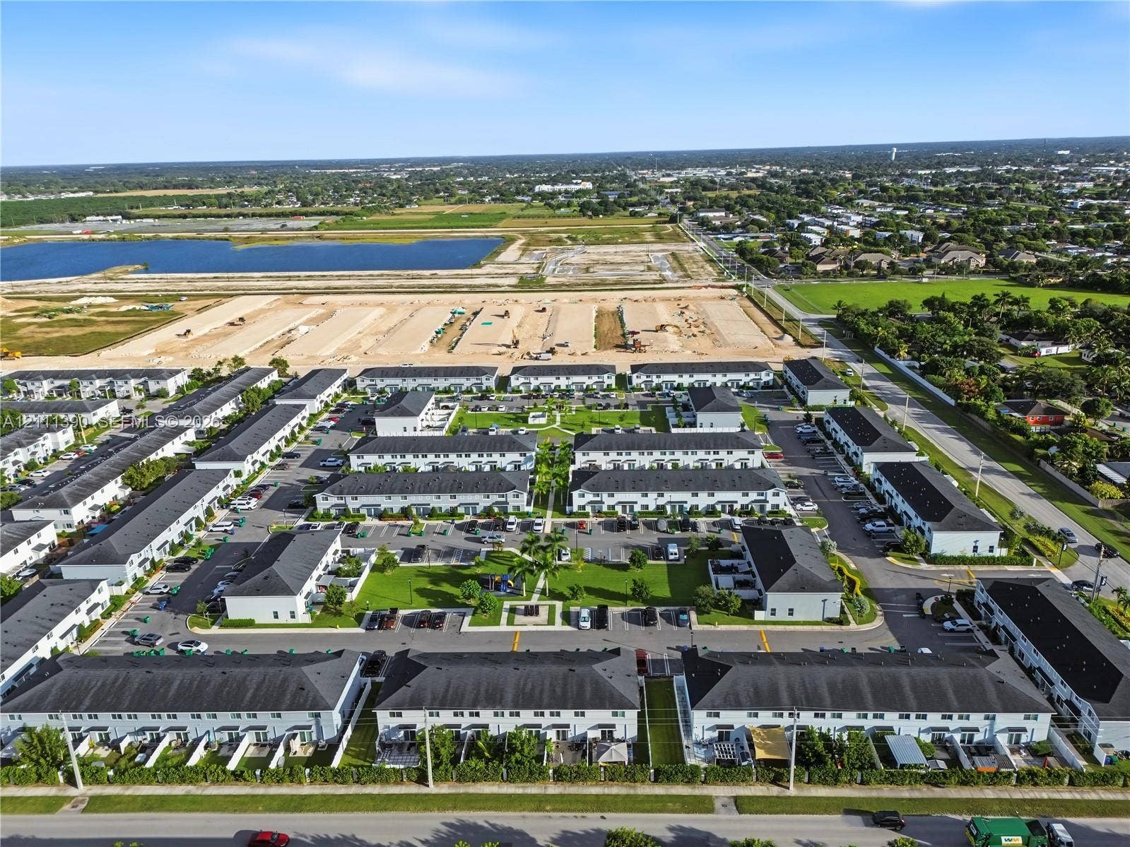 1074 NW 6th Terrace, Florida City, Florida City, FL 33034 Aerial perspective of a townhome community featuring multi-family residential structures with dark shingled roofs, dedicated surface parking, manicured common green spaces, and perimeter landscaping